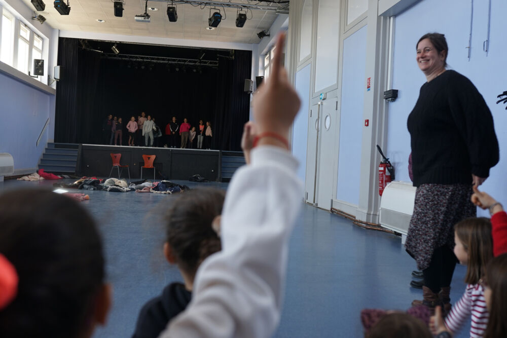 Des enfants jouent une pièce sur la scène de théâtre et d'autres les regardent en posant des questions.