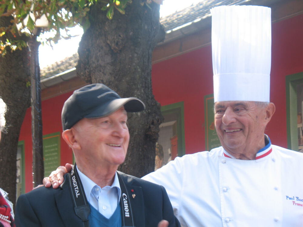 Monsieur Jean-Pierre Haeberlin et Monsieur Paul Bocuse qui se font une accolade et rient ensemble.