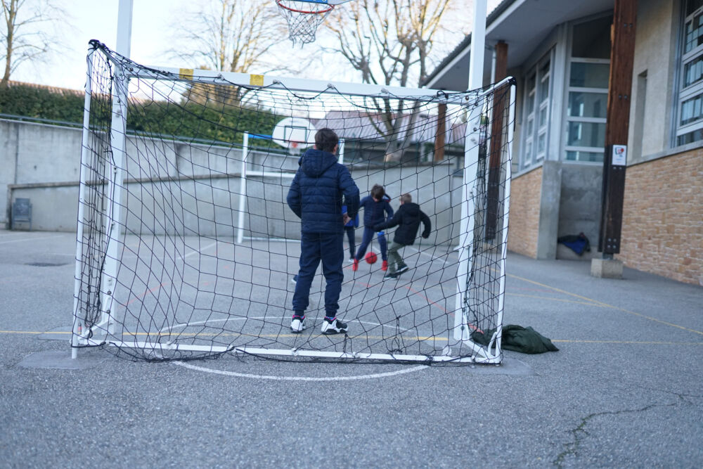 Des enfants jouent au foot sur le terrain de l'école.