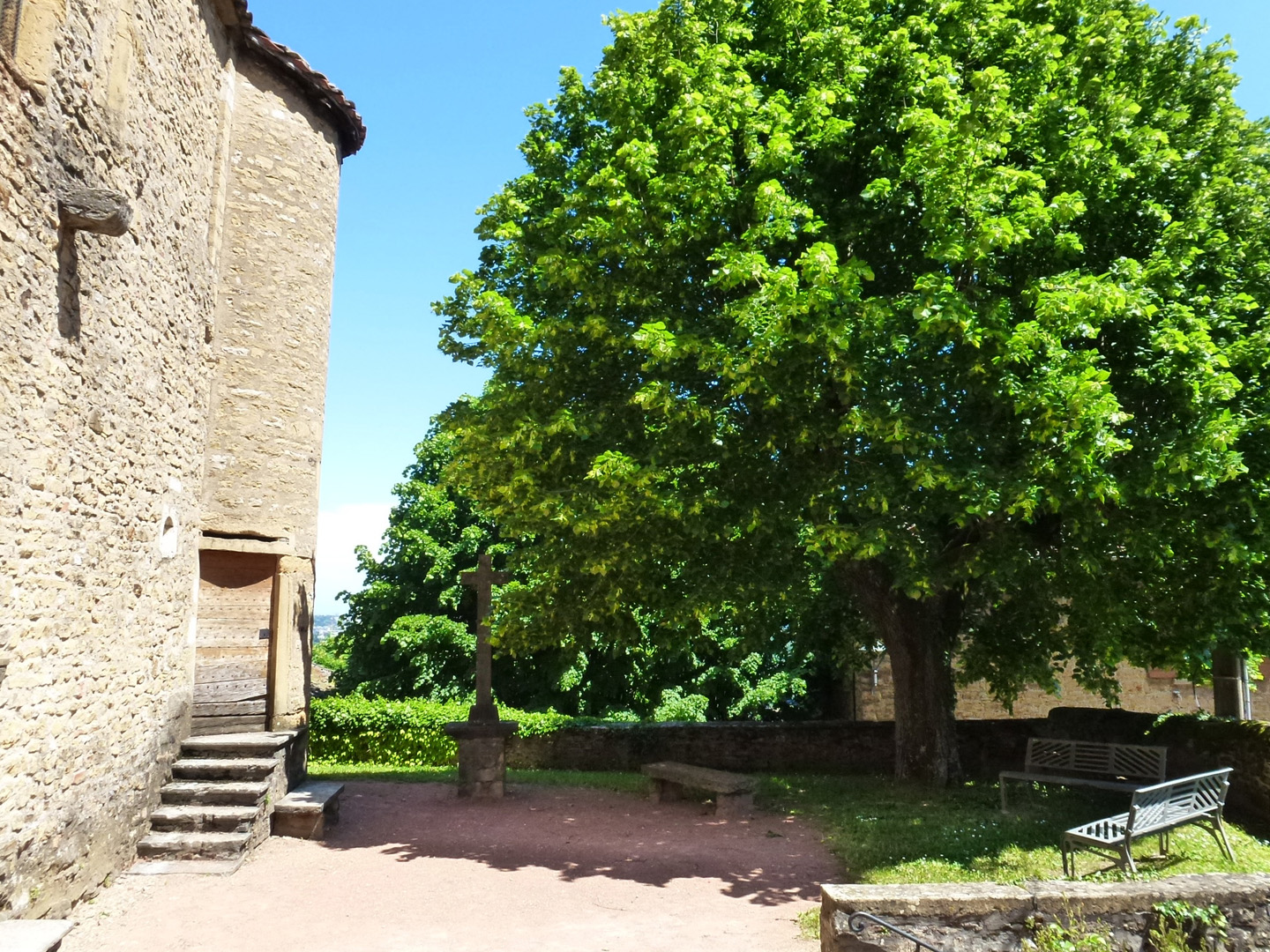 Une photo du parvis de l'église Saint-nizier sur le Mont d'Or au Vieux Collonges. Vous y trouverez l'église en pierre avec un espace vert pour se reposer sous un magnifique tilleul.