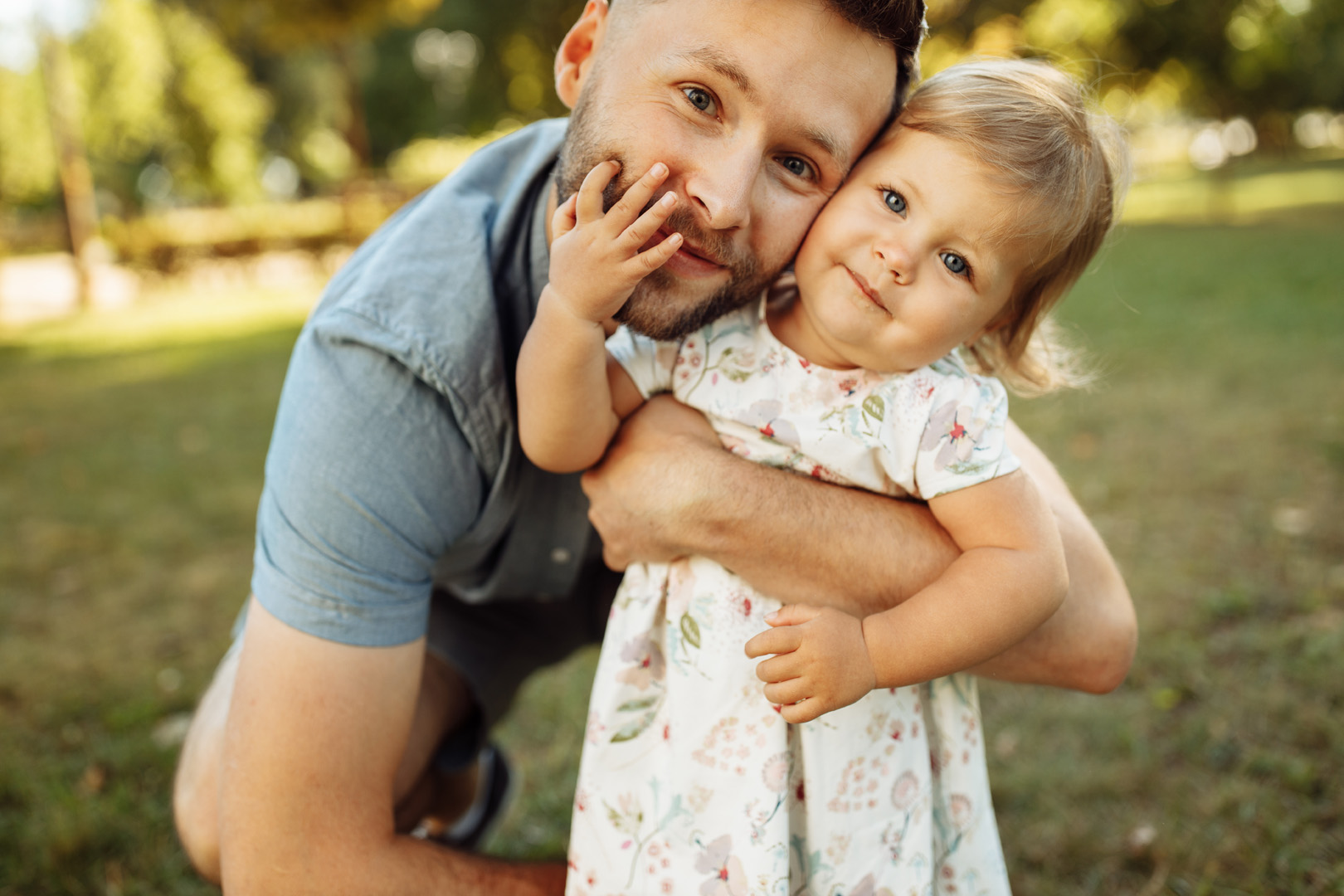 Un homme qui prend un enfant dans ses bras pour lui faire un câlin. La petite fille regarde l'objectif en souriant.