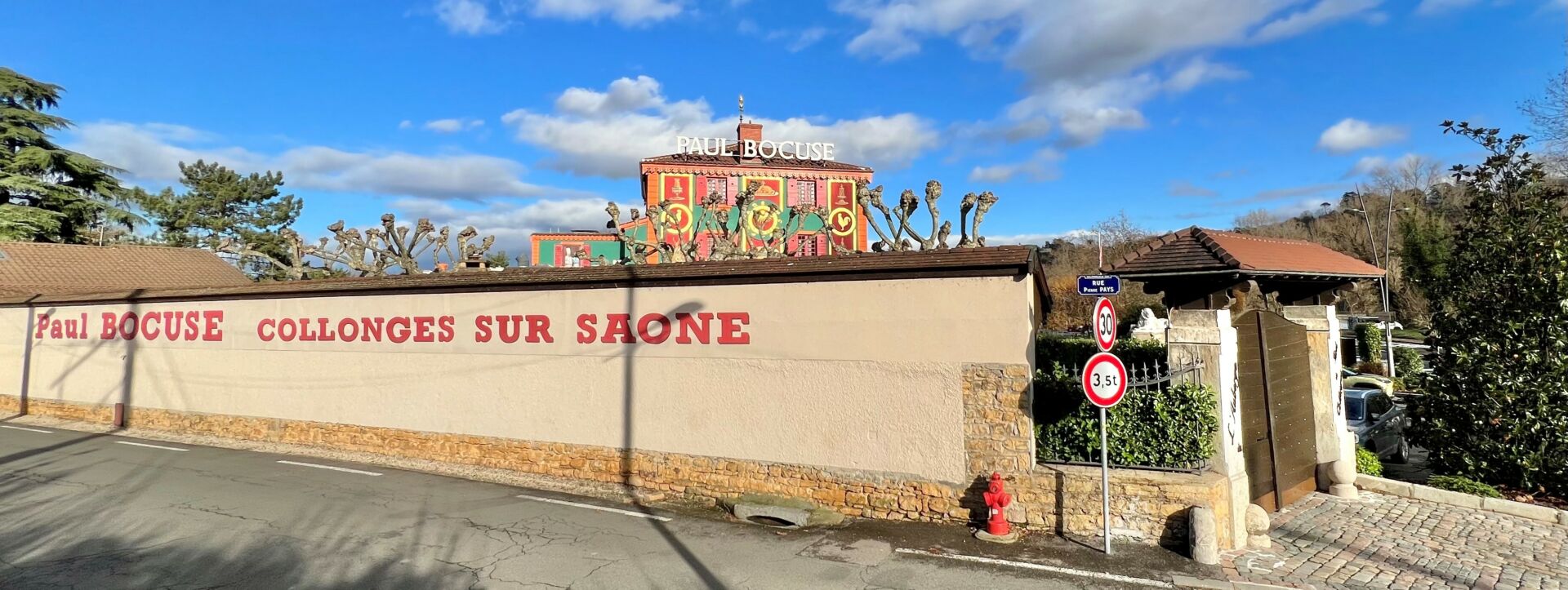 Vue sur le mur d'enceinte du restaurant Paul Bocuse, avec l'auberge en arrière plan