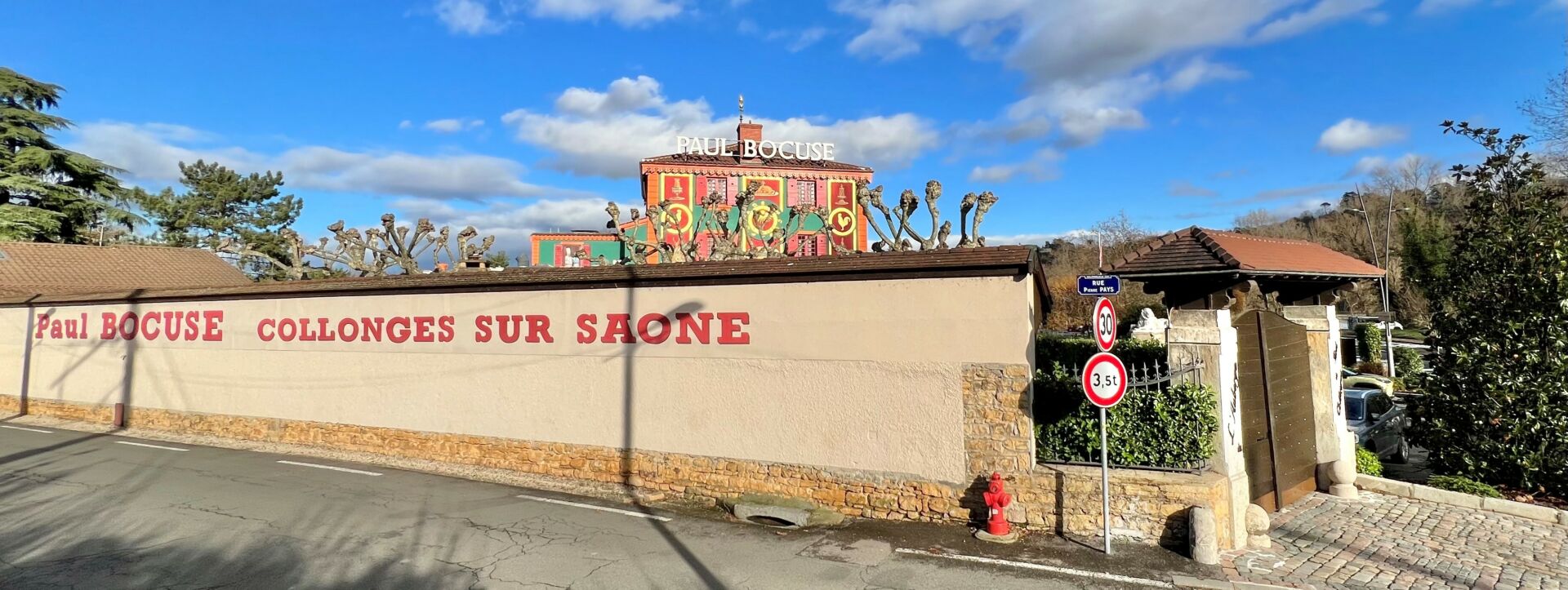 Vue sur le mur d'enceinte du restaurant Paul Bocuse, avec l'auberge en arrière plan